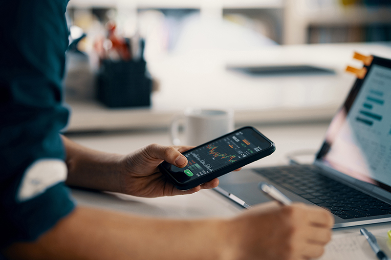 Man looking at charts on smartphone and computer